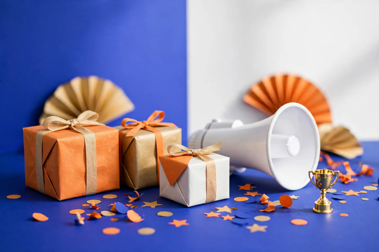 Gift boxes, a megaphone and a trophy on a blue stage